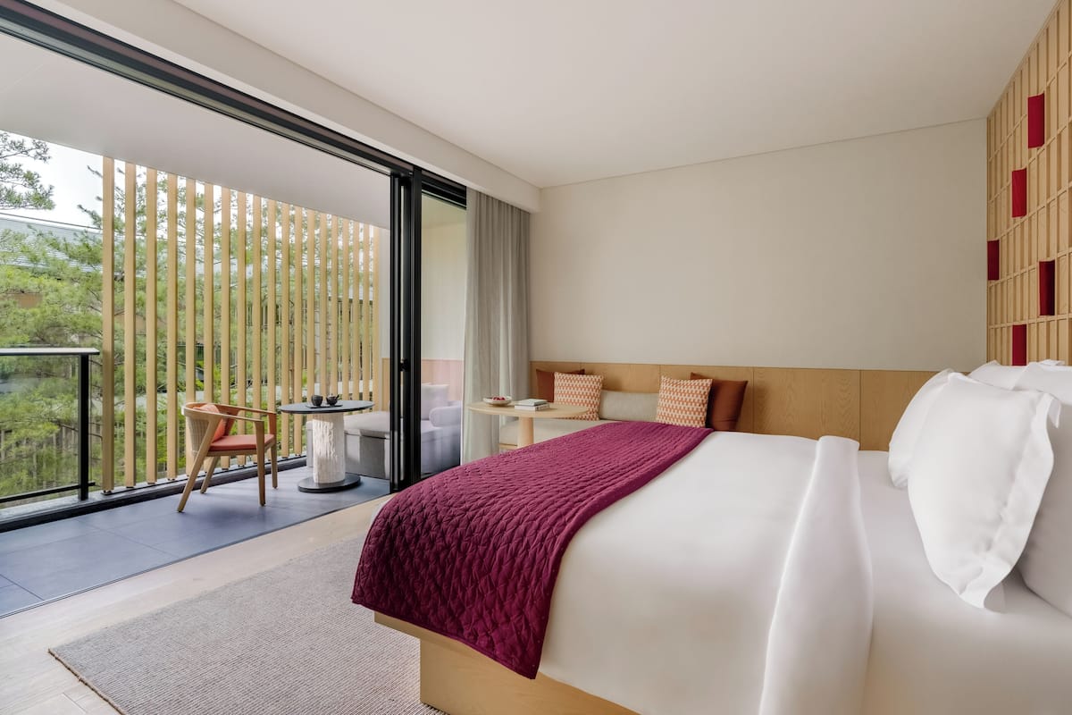 A modern hotel room with a large bed, a small table, and a chair by the balcony.