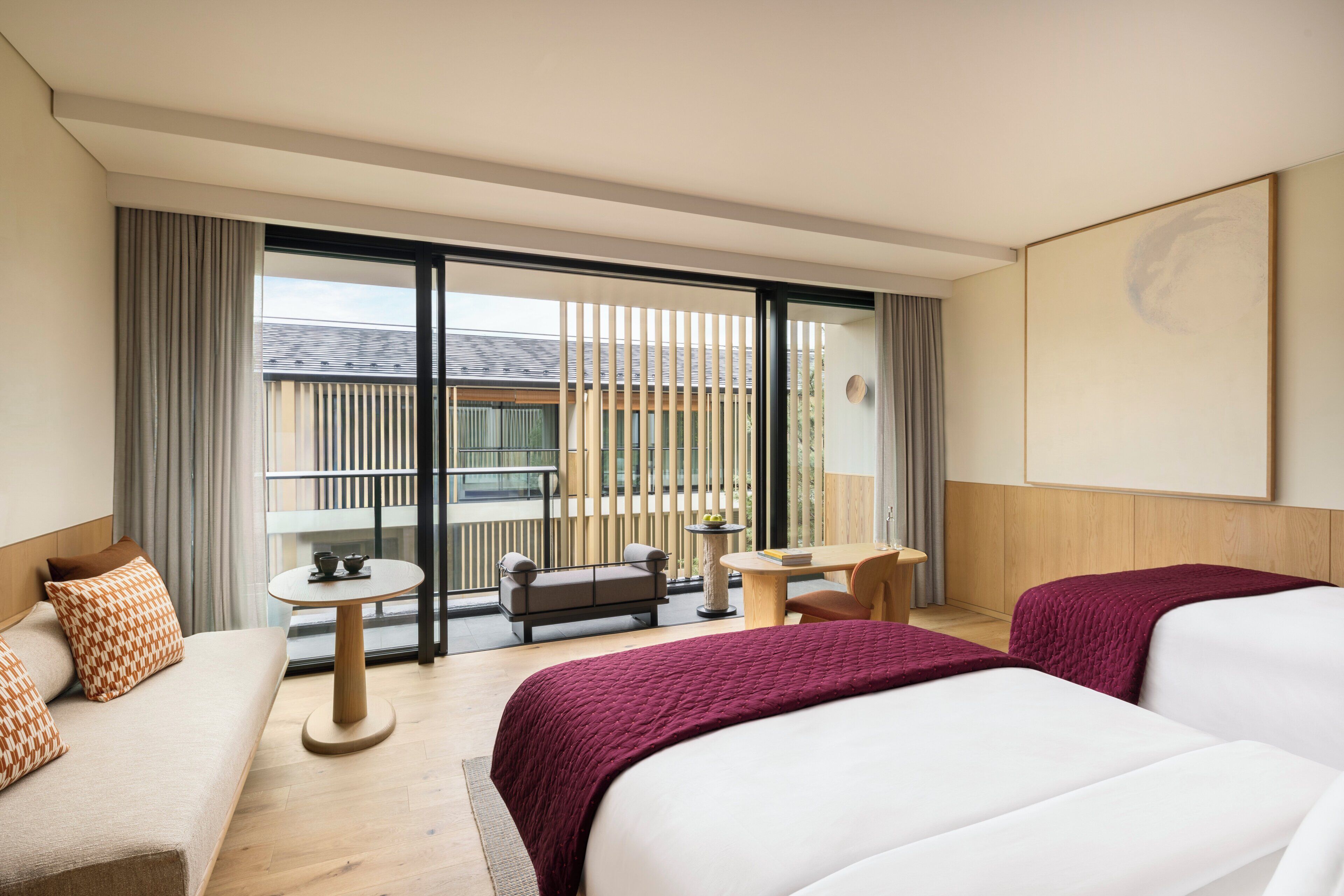 A hotel room with two beds, a sofa, a small table, and a balcony with a view.