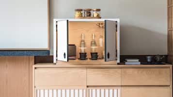 Un armario de cocina de madera con puertas abiertas que muestran botellas de vidrio, frascos y un juego de té.