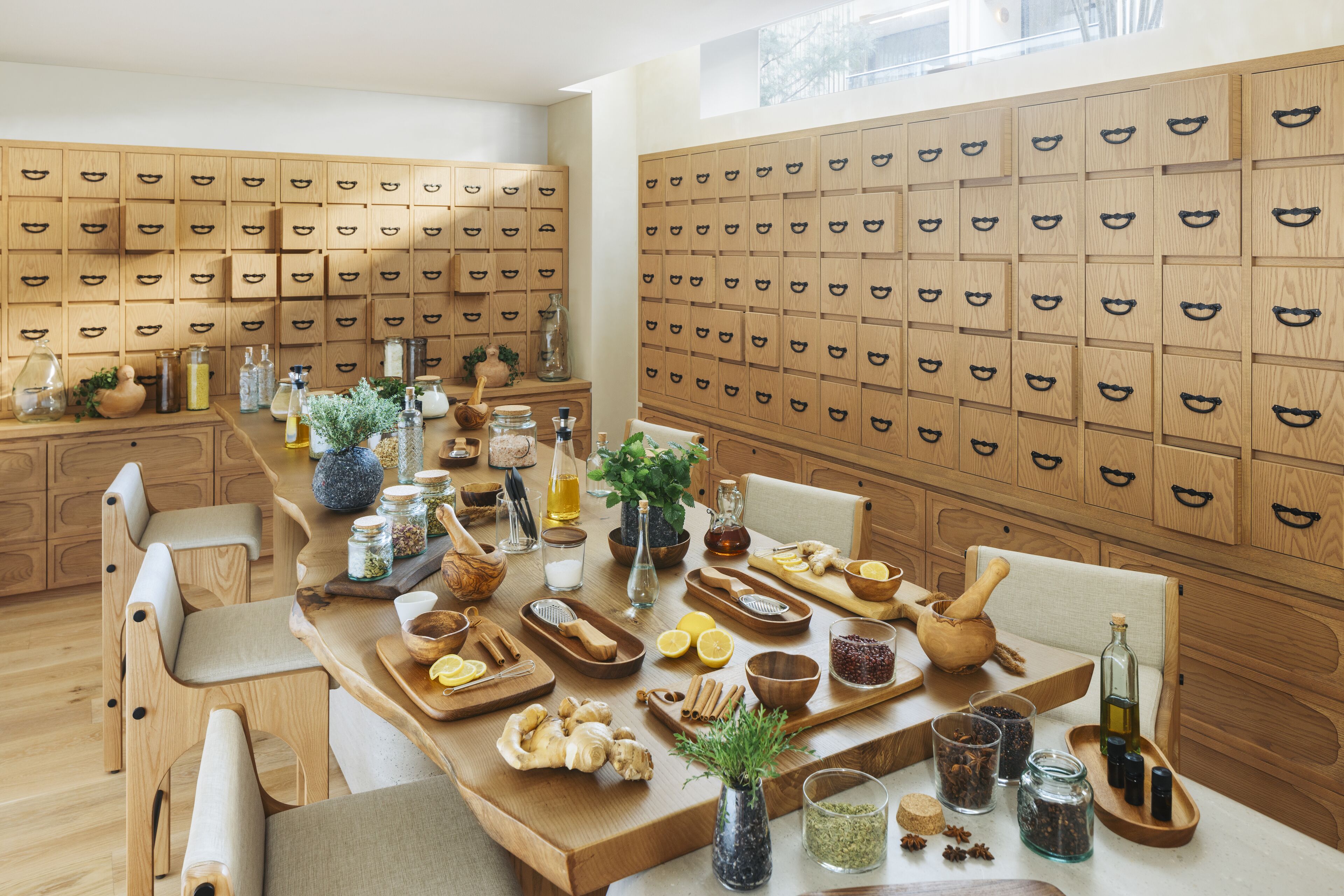 Une cuisine avec des meubles de rangement en bois, une longue table sur laquelle sont disposés divers ustensiles de cuisine, et une grande fenêtre.