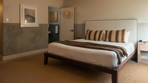 Una cama bien hecha con almohadas a rayas y un cabecero, un cuadro en la pared y una puerta con un letrero.