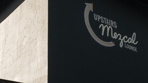 Esquina de un edificio con un cartel que dice "UPSTAIRS Mezcal Lounge".