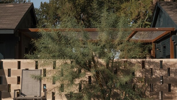 Un edificio moderno con piscina, rodeado de árboles y un muro de piedra.