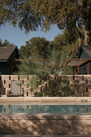 A modern building with a pool, surrounded by trees and a stone wall. - Ranch Motel (San Antonio)