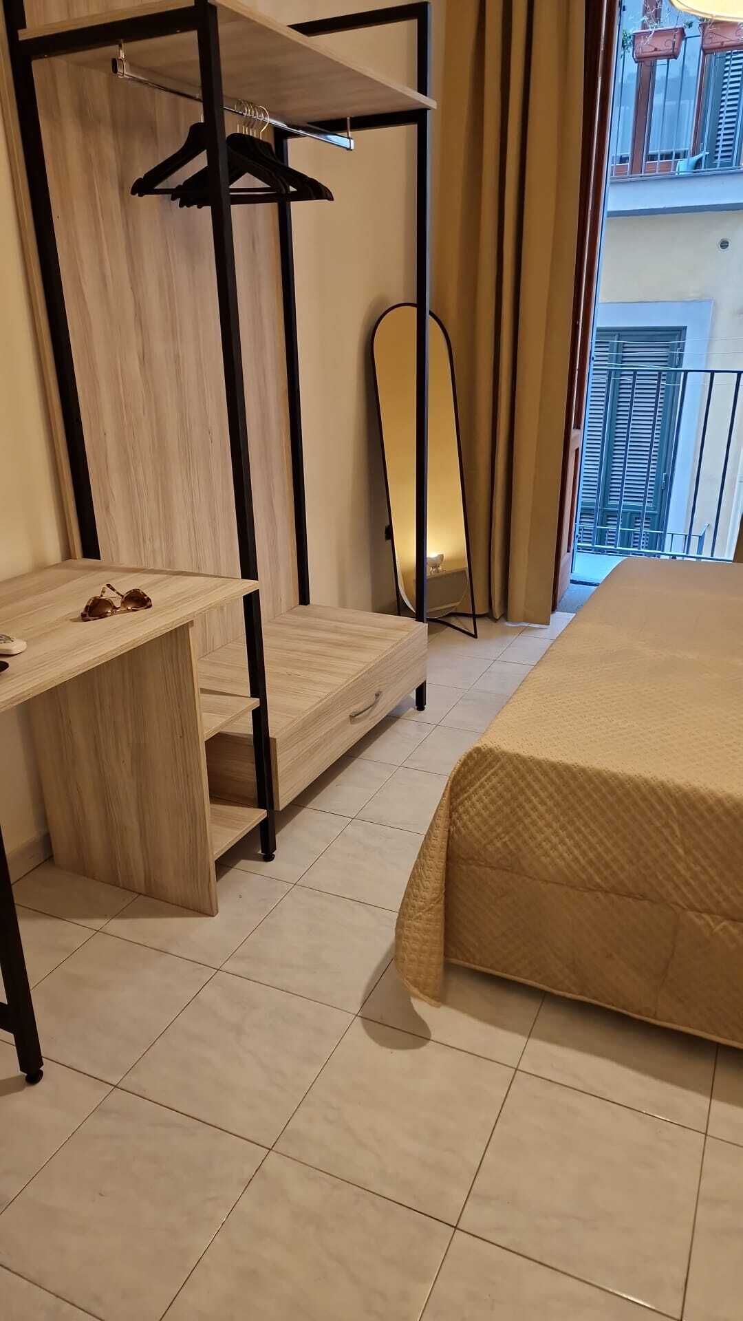 A hotel room with a bed, a wooden desk, a chair, a mirror, and a balcony view.