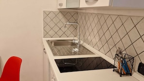 A compact kitchen with a sink, a washing machine, and a red chair. - Incoming Quartieri Spagnoli (Naples)