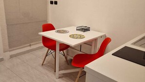 A small, modern kitchen with a white countertop, two red chairs, and a white table. - Incoming Quartieri Spagnoli (Naples)