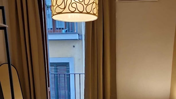 A hotel room with a large bed, a hanging light fixture, an air conditioning unit, and a view of a balcony with a railing. - Incoming Quartieri Spagnoli (Naples)