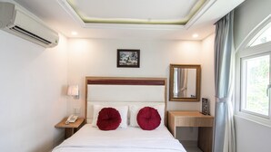 A hotel room with a bed, a bedside table with a lamp, a phone, a mirror, and an air conditioner. - Diamond Hotel (Ho Chi Minh City)