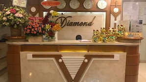 A reception desk with clocks displaying various cities, a 'Happy Birthday' sign, and decorative items including flowers and lucky cat figurines. - Diamond Hotel (Ho Chi Minh City)