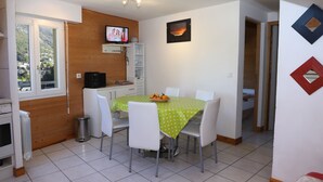 A dining area with a green tablecloth, white chairs, and a TV mounted on the wall. - Appartement Les Pics (Luz-Saint-Sauveur)