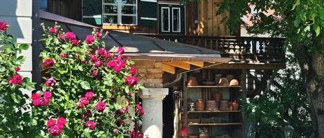 A traditional wooden house with a balcony, a garden with blooming flowers, and a stone pathway.