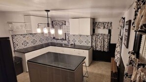 A compact kitchen with a central island, white cabinets, patterned backsplash, and a ceiling light fixture.