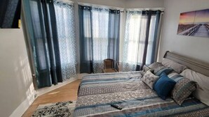 A bedroom with a bed, curtains, a chair, and a painting on the wall.