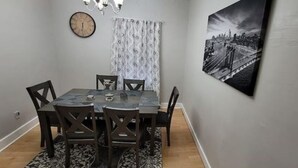 A dining area with a table, chairs, a clock, and a cityscape painting on the wall.