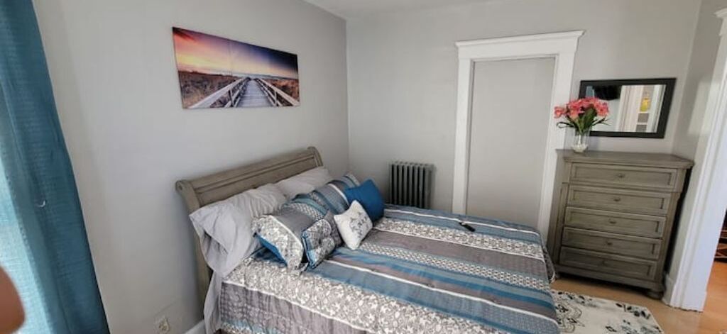 Una camera da letto con un letto, una cassettiera, un termosifone e un quadro appeso al muro.