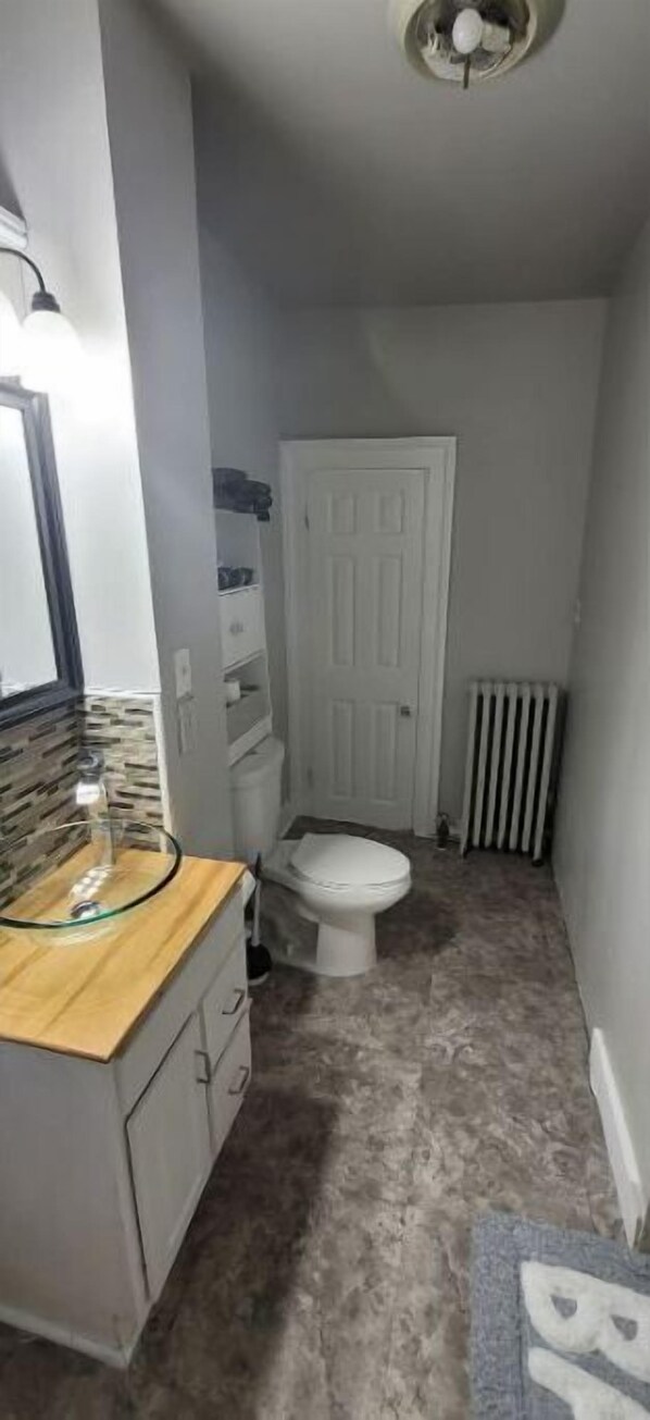 A small bathroom with a toilet, a sink with a glass basin, a white door, and a radiator.