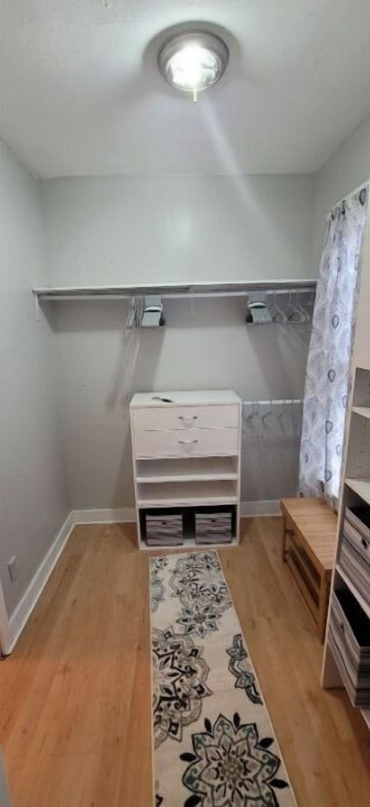 Una habitación pequeña y luminosa con un aparador blanco, una alfombra estampada y un banco de madera.