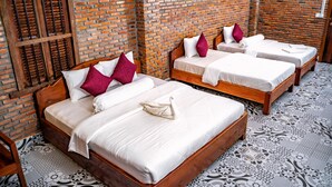 Habitación de hotel con tres camas de madera, cada una con ropa blanca y almohadas rojas y blancas. La habitación tiene una pared de ladrillo y baldosas de suelo estampadas.