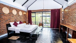 Una habitación con pared de ladrillo, cama con ropa blanca, un banco y una mesa.
