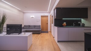 Una sala moderna con un televisor de pantalla plana sobre una mesa blanca, un sofá gris y una puerta de madera al fondo.