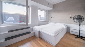 Un dormitorio moderno con cama, ventilador y ventana con vista a la ciudad.