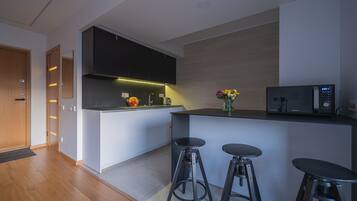 A modern kitchen with a microwave, bar stools, and a fruit bowl.