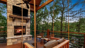 A wooden deck with a stone fireplace, wicker furniture, and a hanging swing.