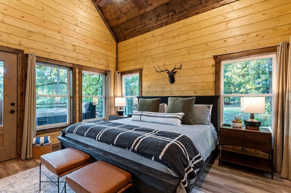 Une chambre dans un chalet en bois, avec un lit, un banc, une table de chevet et une tête de cerf fixée au mur.