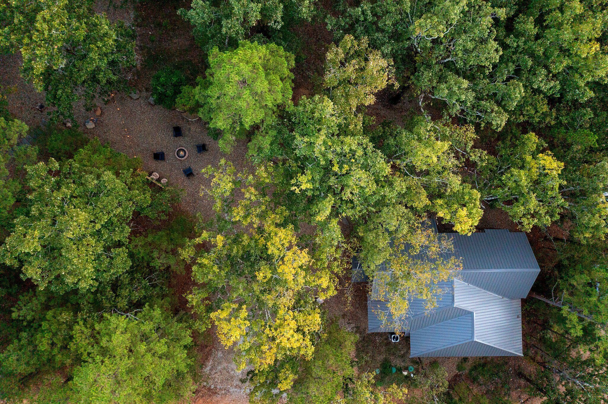 An aerial view of a house surrounded by dense forest, with a clear sky above.