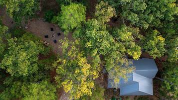 An aerial view of a house surrounded by dense forest, with a clear sky above.