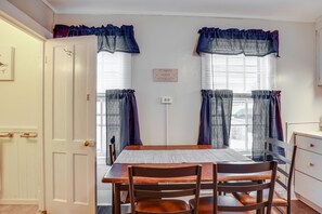 Un comedor con mesa y sillas de madera, una puerta blanca y ventanas con cortinas azules.