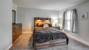 A bedroom with a wooden headboard, a large bed, a nightstand with a lamp, a dresser, and a window with curtains. - Pet-Friendly Auburn Apartment w/ Balcony! (Auburn)