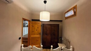 Ein Schlafzimmer mit zwei Einzelbetten, einem Holzschrank, einer Deckenleuchte und einem Fenster mit Vorhängen.