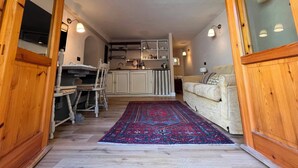 Un salon chaleureux avec un canapé, une table à manger et des chaises, un coin cuisine et un tapis à motifs.
