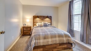 A bedroom with a wooden headboard, a bed with a plaid bedspread, a nightstand with a lamp, and a window with curtains. - Central Auburn Apartment w/ Porch: Pets Welcome! (Auburn)