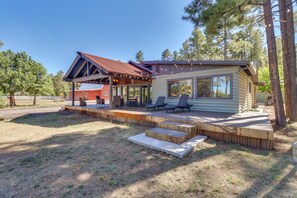 A cabin with a covered porch, outdoor seating, and a view of the surrounding forest. - Fire Pit & Grill: Waterfront Cabin in Lakeside! (Lakeside)