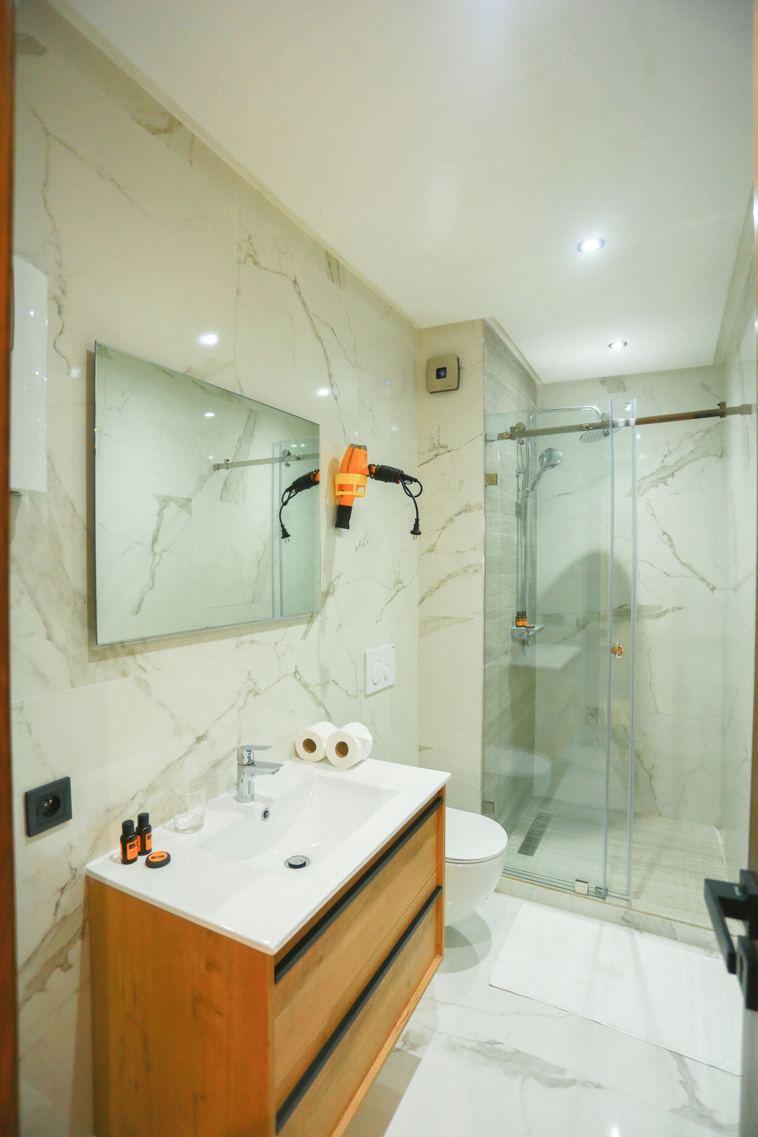 A modern bathroom with a marble vanity, a glass shower enclosure, and a large mirror.