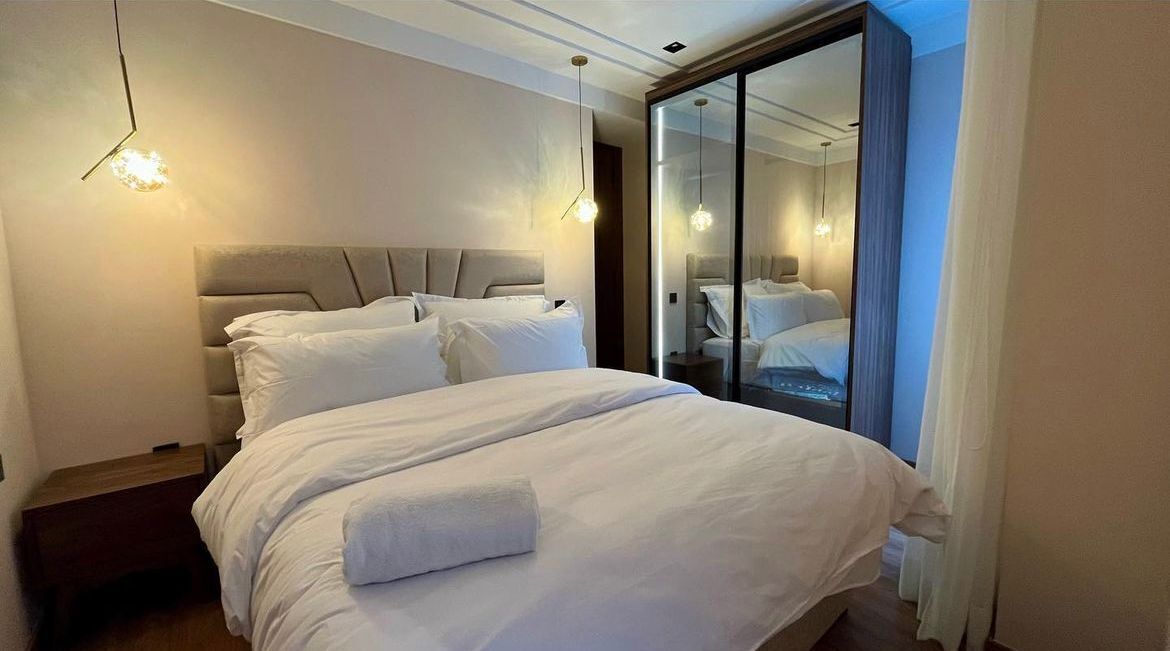 Une chambre d’hôtel moderne avec un grand lit, des tables de chevet et un grand miroir qui reflète la pièce.