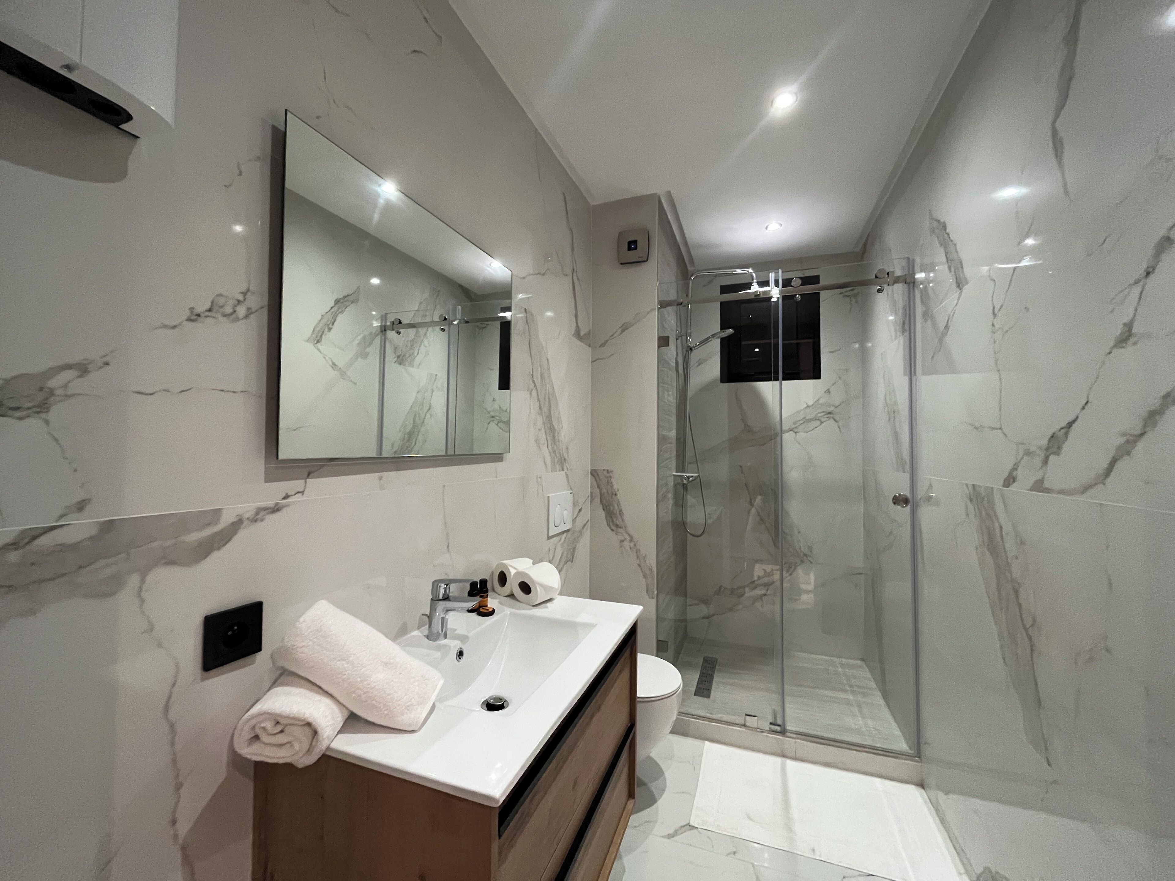 Une salle de bain moderne avec un pare-baignoire en marbre, un grand miroir, un lavabo et une douche à parois de verre.