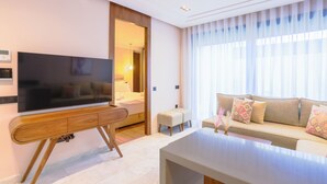 A modern living room with a flat-screen TV, a wooden coffee table, a sofa with patterned cushions, and a large window with sheer curtains. - Les Joyeux Luxury Suites & Appart (Casablanca)