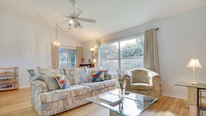 Un salon comprenant un canapé, une table basse en verre, un ventilateur de plafond et une fenêtre avec des rideaux.