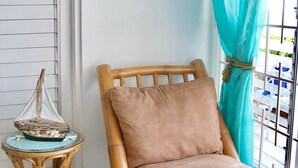 A room with a wooden rocking chair, a small round table with a decorative item, a framed picture on the wall, and a window with a curtain.