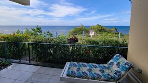 A balcony with a view of the sea, a warning sign, and a lounge chair.