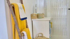 A room with a white door, a white cabinet with a woven basket, and a yellow towel hanging on a wooden stick.