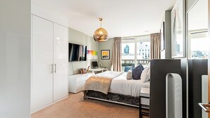 Ein modernes Schlafzimmer mit Bett, Schreibtisch, Stuhl, Kleiderschrank, Fernseher und Blick auf die Stadt.
