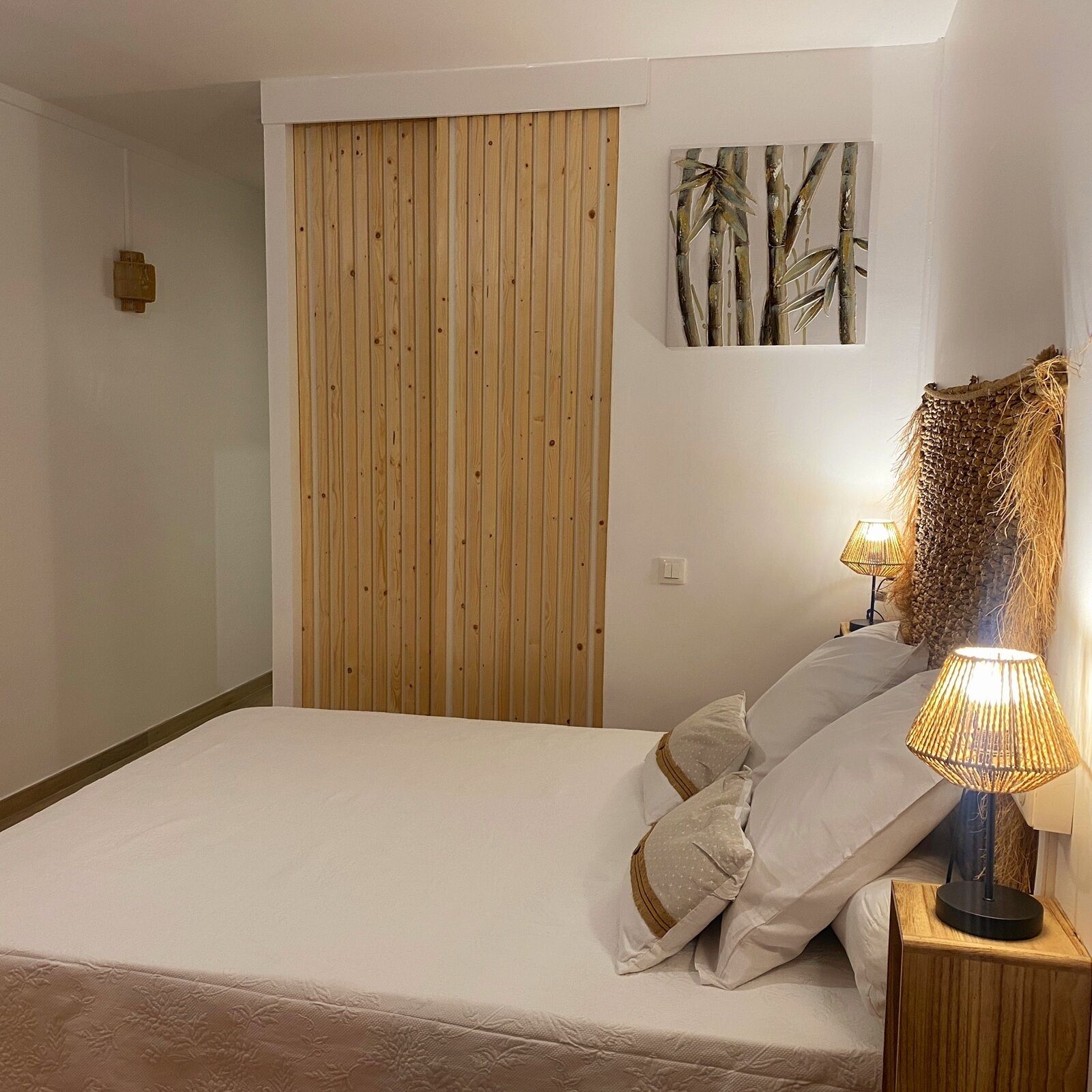 A bedroom with a wooden wardrobe, a bed with white bedding, and a lamp on a bedside table.