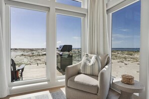 A room with large windows overlooking a beach, a sofa, a small table, and a deck area.