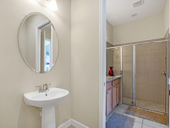 A bathroom with a white sink, a round mirror, and a glass shower enclosure.