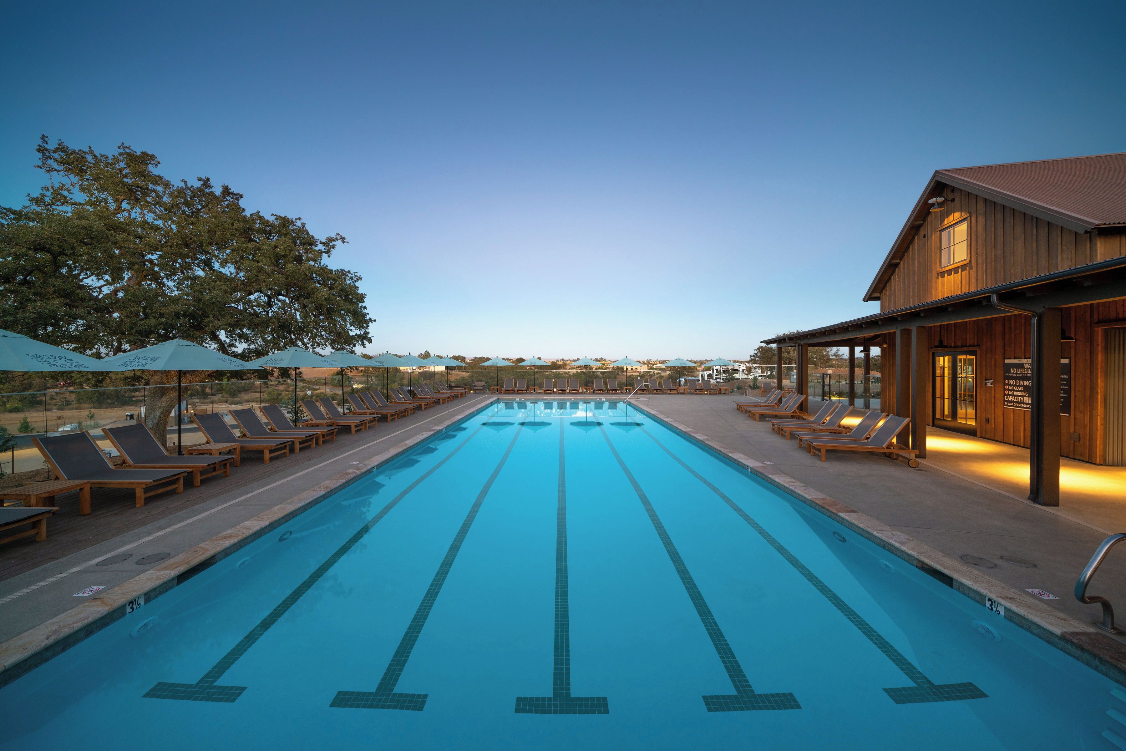 Une piscine entourée de chaises longues et de parasols, elle-même bordée d’un bâtiment en bois doté d’un patio couvert.